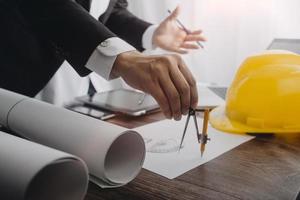 Two colleagues discussing data working and tablet, laptop with on on architectural project at construction site at desk in office photo