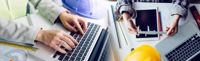 Two colleagues discussing data working and tablet, laptop with on on architectural project at construction site at desk in office photo