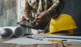 Two colleagues discussing data working and tablet, laptop with on on architectural project at construction site at desk in office photo