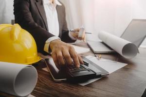 Two colleagues discussing data working and tablet, laptop with on on architectural project at construction site at desk in office photo