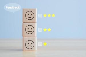 experiencia de calificación de servicio al cliente o de negocios y concepto de encuesta de satisfacción y emoción de retroalimentación. cubo de madera encuesta de satisfacción con estrella y expresiones faciales negativas, neutras y positivas. foto