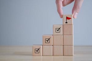 Checklist Survey and assessment. quality Control. Goals achievement and business success. Hand Holding wooden block with red flag icon and check mark on cube ladder. photo