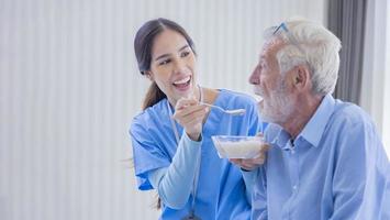 Hospice nurse is feeding porridge food to Caucasian man at pension retirement center for home care rehabilitation and post treatment recovery process photo