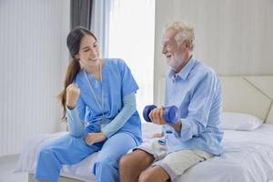 Hospice nurse is helping Caucasian man in bed to exercising muscle strength in pension retirement center for home care rehabilitation and post treatment recovery process photo