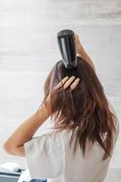 young woman using hair dryer at home or hotel. Hairstyles and lifestyle concepts photo