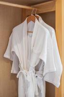 White clean bathrobe hanging in wooden wardrobe at luxury hotel or home. Relax and travel concept photo