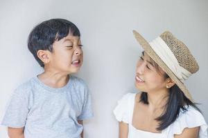 retrato hermosa viajera madre asiática con vestido blanco, sombrero de paja e hijo con camisa gris disfruta de una sonrisa relajada en el resort en vacaciones en la playa tropical foto