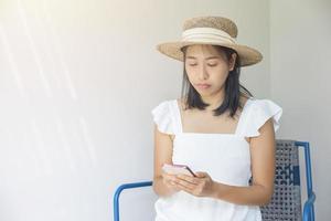 foto de una joven feliz con un vestido blanco y un sombrero de paja con una sonrisa positiva que usa el teléfono inteligente. concepto de social, tecnología, viajes, descanso.