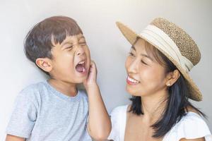 Portrait beautiful traveler asian mother in white dress, straw hat and son in grey shirt enjoys relax smile leisure at resort in tropical beach vacation photo