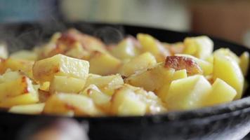 roosteren vers aardappelen in een gips ijzer koekepan met zonnebloem olie. een visie van een fornuis met een frituren pan gevulde met gouden gebakken aardappelen in een echt keuken. voedsel gekookt in een eigengemaakt frituren pan. video