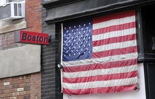 A sign with the word Boston next to an American flag over a window photo