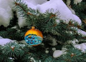 Christmas ball hanging on a snow-covered branch of a Christmas tree on a festive background of white snow and snowy bokeh with copy space. photo