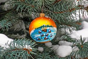 Christmas ball hanging on a snow-covered branch of a Christmas tree on a festive background of white snow and snowy bokeh with copy space. photo