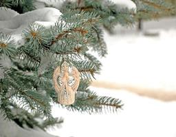 ángel de juguete de navidad cuelga de una rama cubierta de nieve de un árbol de navidad sobre un fondo festivo de nieve blanca bokeh con espacio para copiar. foto