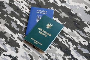 Ukrainian military ID and foreign passport on fabric with texture of pixeled camouflage. Cloth with camo pattern in grey, brown and green shapes with Ukrainian army personal token and passport. photo