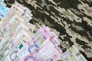 Ukrainian hryvnya bills on fabric with texture of Ukrainian military pixeled camouflage. Cloth with camo pattern in grey, brown and green pixel shapes photo