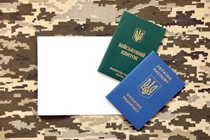 Ukrainian military ID and foreign passport on fabric with texture of pixeled camouflage. Cloth with camo pattern in grey, brown and green shapes with Ukrainian army personal token and passport. photo