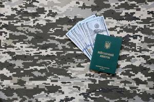 Ukrainian military ID and US dollar bills on fabric with texture of pixeled camouflage. Cloth with camo pattern in grey, brown and green pixel shapes with Ukrainian army personal token. photo