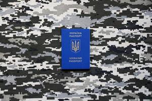 Ukrainian foreign passport on fabric with texture of military pixeled camouflage. Cloth with camo pattern in grey, brown and green pixel shapes and Ukrainian ID photo