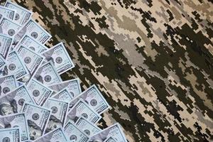 US dollar bills on fabric with texture of Ukrainian military pixeled camouflage. Cloth with camo pattern in grey, brown and green pixel shapes photo