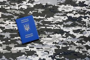 Ukrainian foreign passport on fabric with texture of military pixeled camouflage. Cloth with camo pattern in grey, brown and green pixel shapes and Ukrainian ID photo