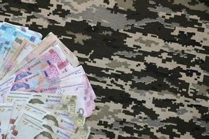 Ukrainian hryvnya bills on fabric with texture of Ukrainian military pixeled camouflage. Cloth with camo pattern in grey, brown and green pixel shapes photo
