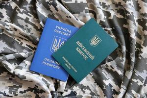 Ukrainian military ID and foreign passport on fabric with texture of pixeled camouflage. Cloth with camo pattern in grey, brown and green shapes with Ukrainian army personal token and passport. photo