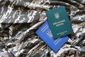 Ukrainian military ID and foreign passport on fabric with texture of pixeled camouflage. Cloth with camo pattern in grey, brown and green shapes with Ukrainian army personal token and passport. photo