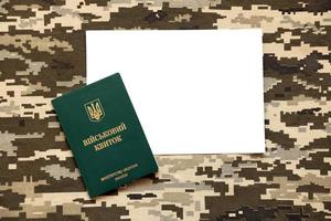 Ukrainian military ID and blank paper sheet on fabric with texture of pixeled camouflage. Cloth with camo pattern in grey, brown and green pixel shapes with Ukrainian army personal token. photo