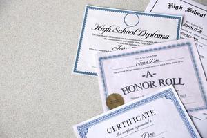 A honor roll recognition, certificate of achievement and high school diploma lies on table. Education documents photo