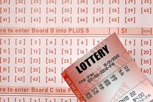 Red lottery ticket lies on pink gambling sheets with numbers for marking to play lottery. Lottery playing concept or gambling addiction. Close up photo