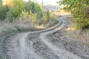 Autumn landscape with a curved road and traces of the tread of large wheels of agricultural machinery photo