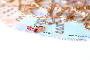 Many expensive golden jewerly rings, earrings and necklaces with big amount of Ukrainian money bills. Pawnshop or jewerly shop concept. Jewelry trading photo