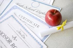 un reconocimiento del cuadro de honor, un certificado de logros y un diploma de escuela secundaria se encuentran en la mesa con un pequeño pergamino y una manzana roja. documentos educativos foto