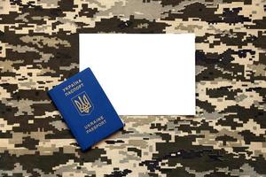 Ukrainian foreign passport on fabric with texture of military pixeled camouflage. Cloth with camo pattern in grey, brown and green pixel shapes and Ukrainian ID photo