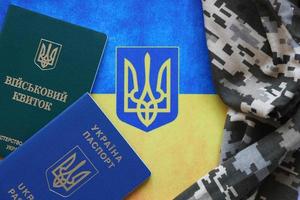 Ukrainian military ID and foreign passport on fabric with texture of pixeled camouflage. Cloth with camo pattern in grey, brown and green shapes with Ukrainian army personal token and passport. photo