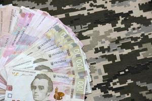 Ukrainian hryvnya bills on fabric with texture of Ukrainian military pixeled camouflage. Cloth with camo pattern in grey, brown and green pixel shapes photo
