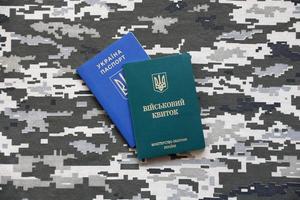 Ukrainian military ID and foreign passport on fabric with texture of pixeled camouflage. Cloth with camo pattern in grey, brown and green shapes with Ukrainian army personal token and passport. photo