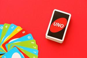 Many colorful UNO game cards on red background. UNO is an American shedding-type card game that is played with a specially printed deck photo