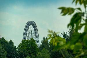 landscape of an amusement park with the top of a Ferris wheel showing above the tree tops against a blue sky. photo