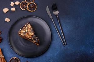 A piece of fresh delicious cake with nuts and chocolate on a black plate against a dark blue background photo