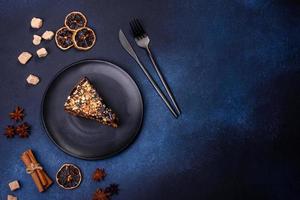 A piece of fresh delicious cake with nuts and chocolate on a black plate against a dark blue background photo