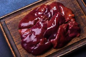 Pieces of raw liver on a wooden cutting board against a dark concrete background photo