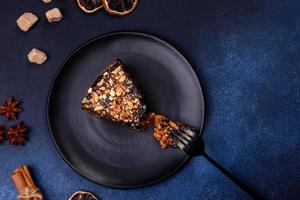 A piece of fresh delicious cake with nuts and chocolate on a black plate against a dark blue background photo