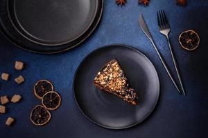 A piece of fresh delicious cake with nuts and chocolate on a black plate against a dark blue background photo