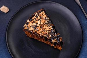 A piece of fresh delicious cake with nuts and chocolate on a black plate against a dark blue background photo