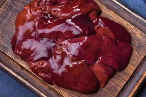 Pieces of raw liver on a wooden cutting board against a dark concrete background photo