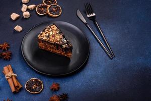 A piece of fresh delicious cake with nuts and chocolate on a black plate against a dark blue background photo