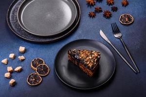 A piece of fresh delicious cake with nuts and chocolate on a black plate against a dark blue background photo