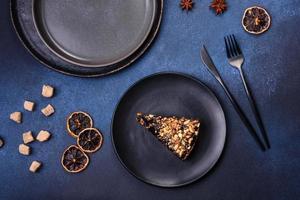 A piece of fresh delicious cake with nuts and chocolate on a black plate against a dark blue background photo